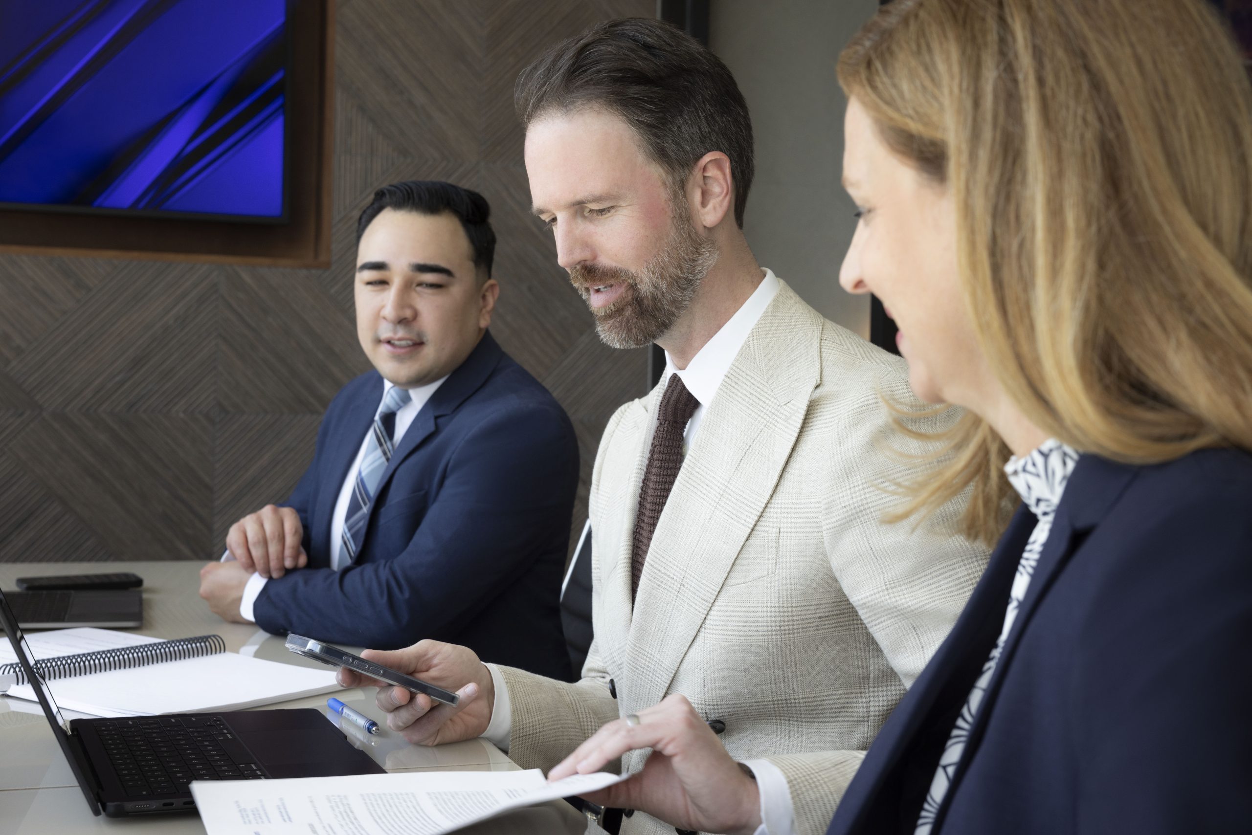 Three professionals collaborating in an office, with one reviewing documents and another using a phone